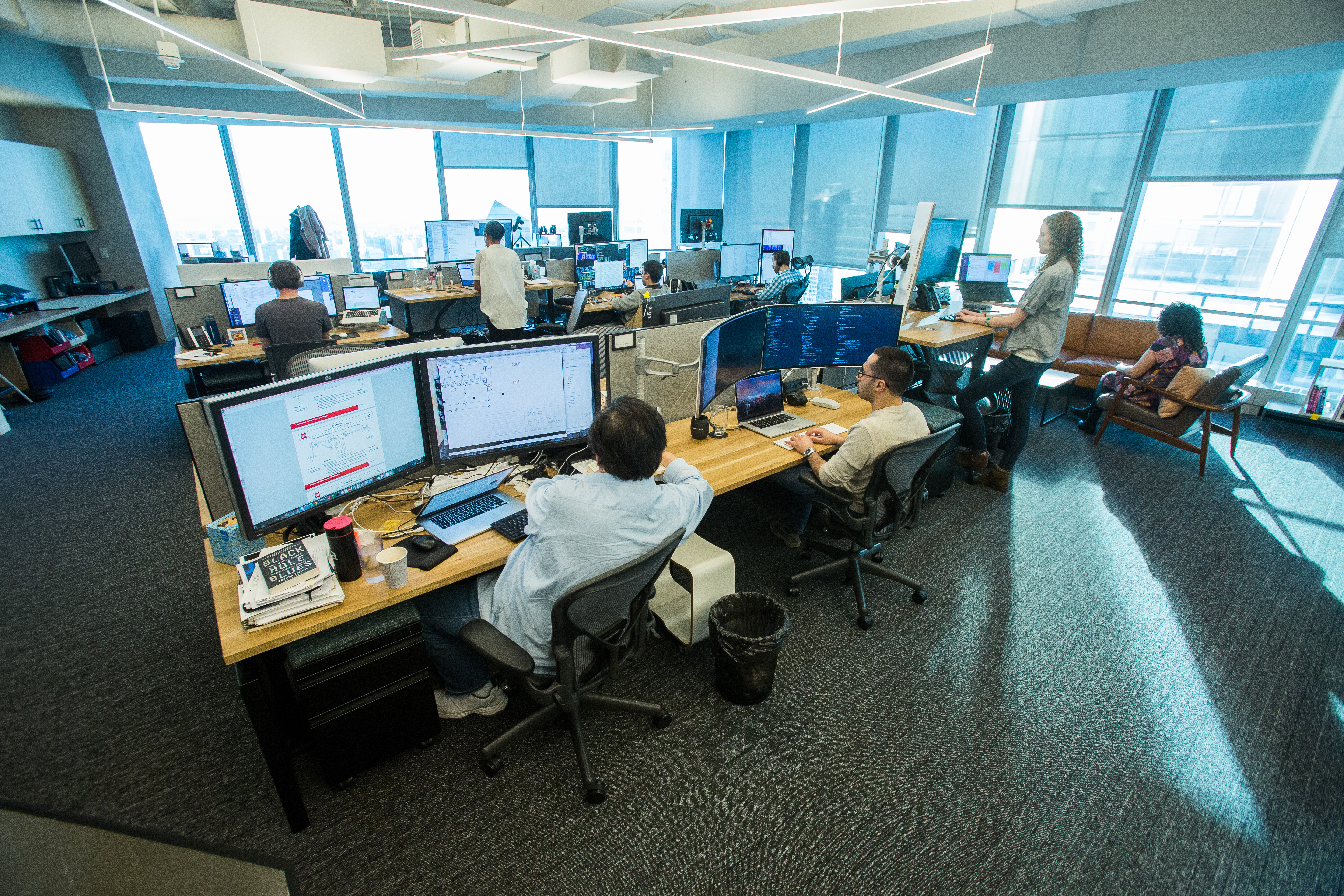 HRT trading floor: rows of desks with multiple monitors, people working under blue-tinted natural light