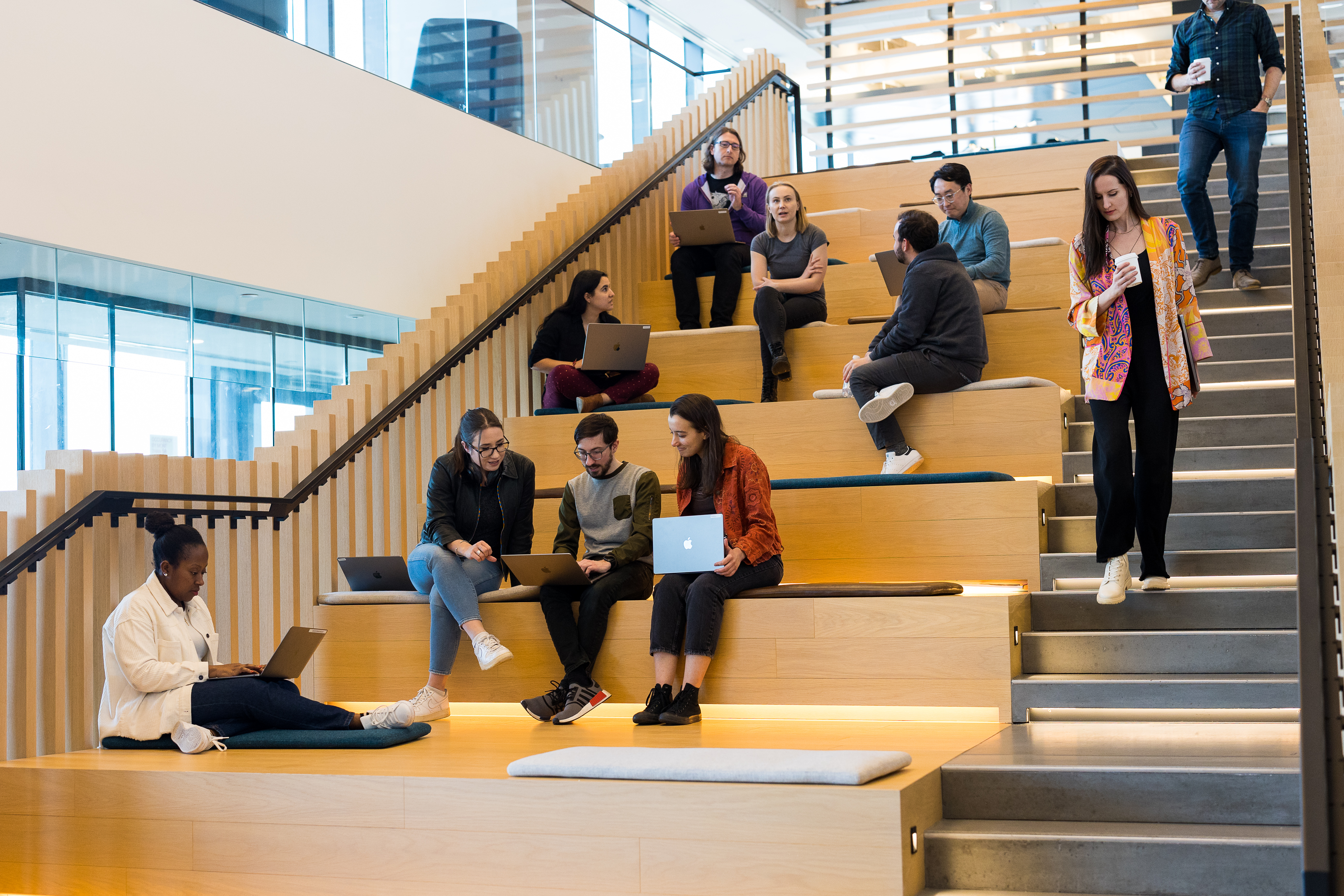 HRT office: people sitting on a wide wooden amphitheater staircase, working on laptops